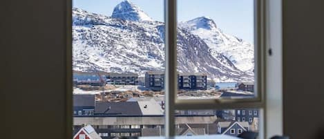 A room with a large window offering a view of a snowy mountain and buildings.