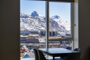 A room with a large window offering a view of a snowy mountain and buildings.