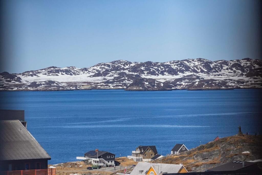Une ville côtière avec des maisons situées près d’une étendue d’eau importante et des montagnes enneigées en arrière-plan.