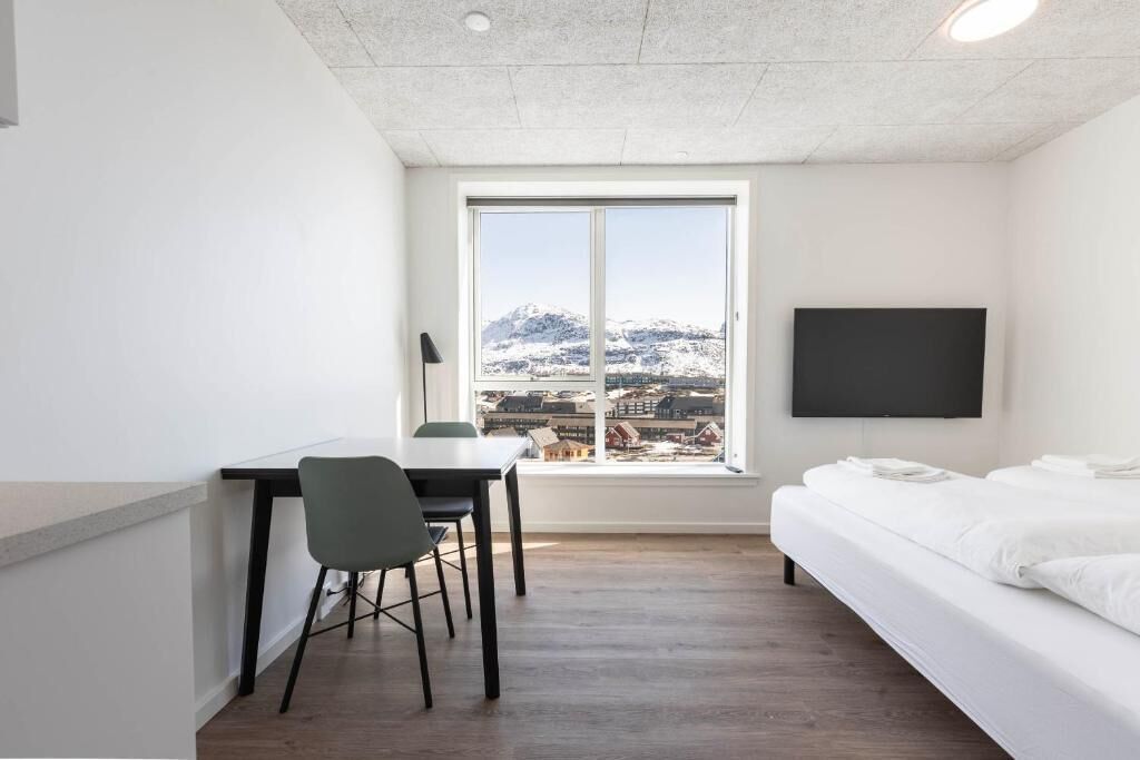Ein Zimmer mit einem Bett, einem Schreibtisch, einem Stuhl, einem Fernseher und einem Fenster mit Blick auf verschneite Berge.