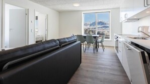 Une cuisine moderne avec un coin repas, un canapé noir et une vue sur une montagne enneigée.
