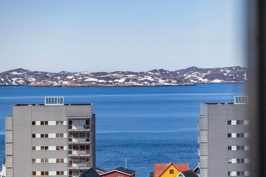 A high-rise building with multiple floors and balconies, overlooking a body of water and a mountainous landscape.