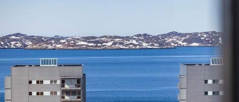 A high-rise building with multiple floors and balconies, overlooking a body of water and a mountainous landscape.