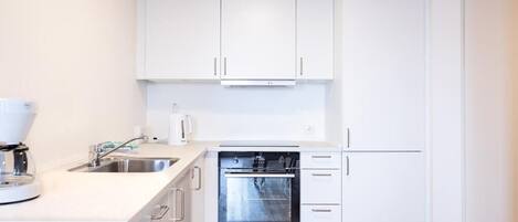 A modern kitchen with white cabinets, a built-in oven, and a coffee maker.