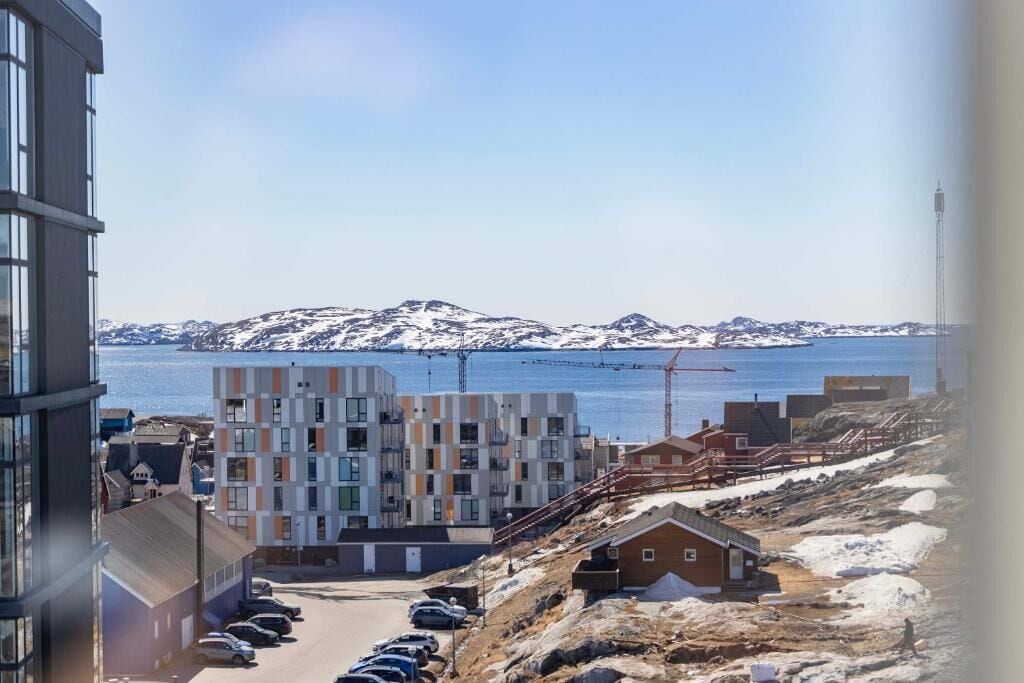 A coastal building complex with multiple floors, a parking area, and a view of the sea and mountains.