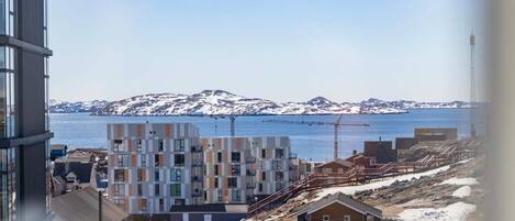 A coastal building complex with multiple floors, a parking area, and a view of the sea and mountains.