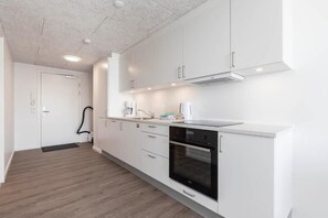 A modern kitchen with white cabinets, a built-in oven, and a coffee maker. - Aurora City Apartments (Nuuk)