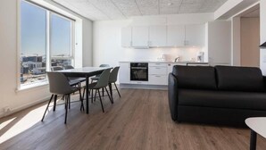 Una cocina moderna con armarios blancos, un comedor con mesa y sillas, y un sofá negro.
