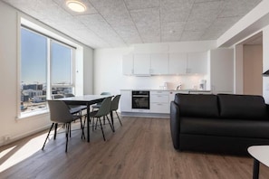 Una cocina moderna con armarios blancos, un comedor con mesa y sillas, y un sofá negro.