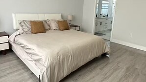 Ein Schlafzimmer mit einem Bett, Nachttischen, einem Deckenventilator und Blick ins Badezimmer.