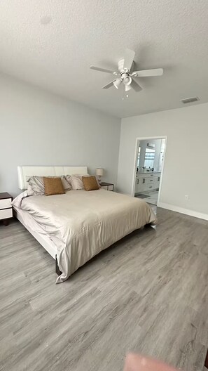 Ein Schlafzimmer mit einem Bett, Nachttischen, einem Deckenventilator und Blick ins Badezimmer.