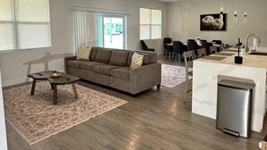 Ein modernes Wohnzimmer mit Sofa, Couchtisch und einer Küchenzeile mit Kühlschrank.
