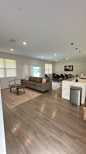 Ein modernes Wohnzimmer mit Sofa, Couchtisch und einer Küchenzeile mit Kühlschrank.