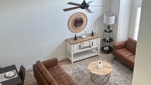 A modern living room with a brown sofa, a round coffee table, a white console table, a ceiling fan, and a lamp. - Beach House (Indialantic)
