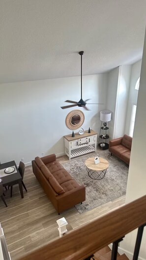 Un salon moderne avec un canapé marron, une table basse ronde, une console blanche, un ventilateur de plafond et une lampe.