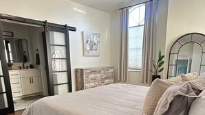A bedroom with a bed, a ceiling fan, a dresser, a mirror, and a window with curtains. - Beach House (Indialantic)