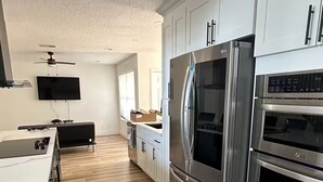 A modern kitchen with white cabinetry, stainless steel appliances, and a wooden floor. - Beach House (Indialantic)