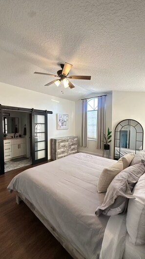 Ein Schlafzimmer mit einem großen Bett, einem Deckenventilator, einem Schiebetürenschrank und einem Fenster mit Vorhängen.