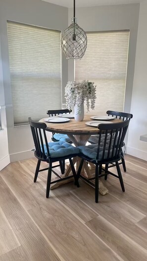 Une table à manger avec des chaises, un luminaire suspendu et un vase rempli de fleurs.