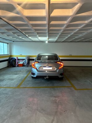 A parking garage with a car parked in a marked space, concrete floor, and a ceiling with a grid pattern.