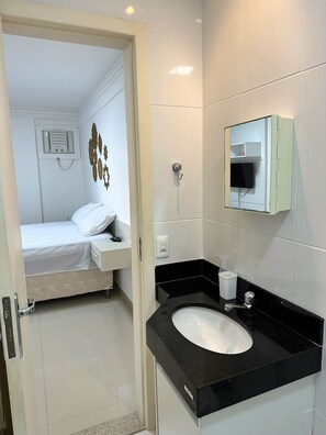Ein Hotelzimmer mit Bett, Badezimmer mit Waschbecken und einem an der Wand befestigten Fernseher.