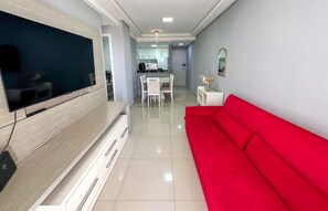 Un salon moderne avec un téléviseur à écran plat, un canapé rouge et un coin repas avec des chaises blanches.