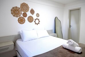 A hotel room with a neatly made bed, a wall with decorative cut-out patterns, a surfboard leaning against the wall, and a door. - 3 bedrooms with the best location in Guarapari (Guarapri)