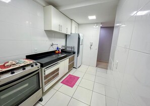 A compact kitchen with white cabinets, a stove, a refrigerator, and a small countertop. - 3 bedrooms with the best location in Guarapari (Guarapri)