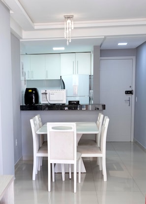 A modern kitchen with white cabinets, a black countertop, and a dining area with a white table and chairs. - 3 bedrooms with the best location in Guarapari (Guarapri)