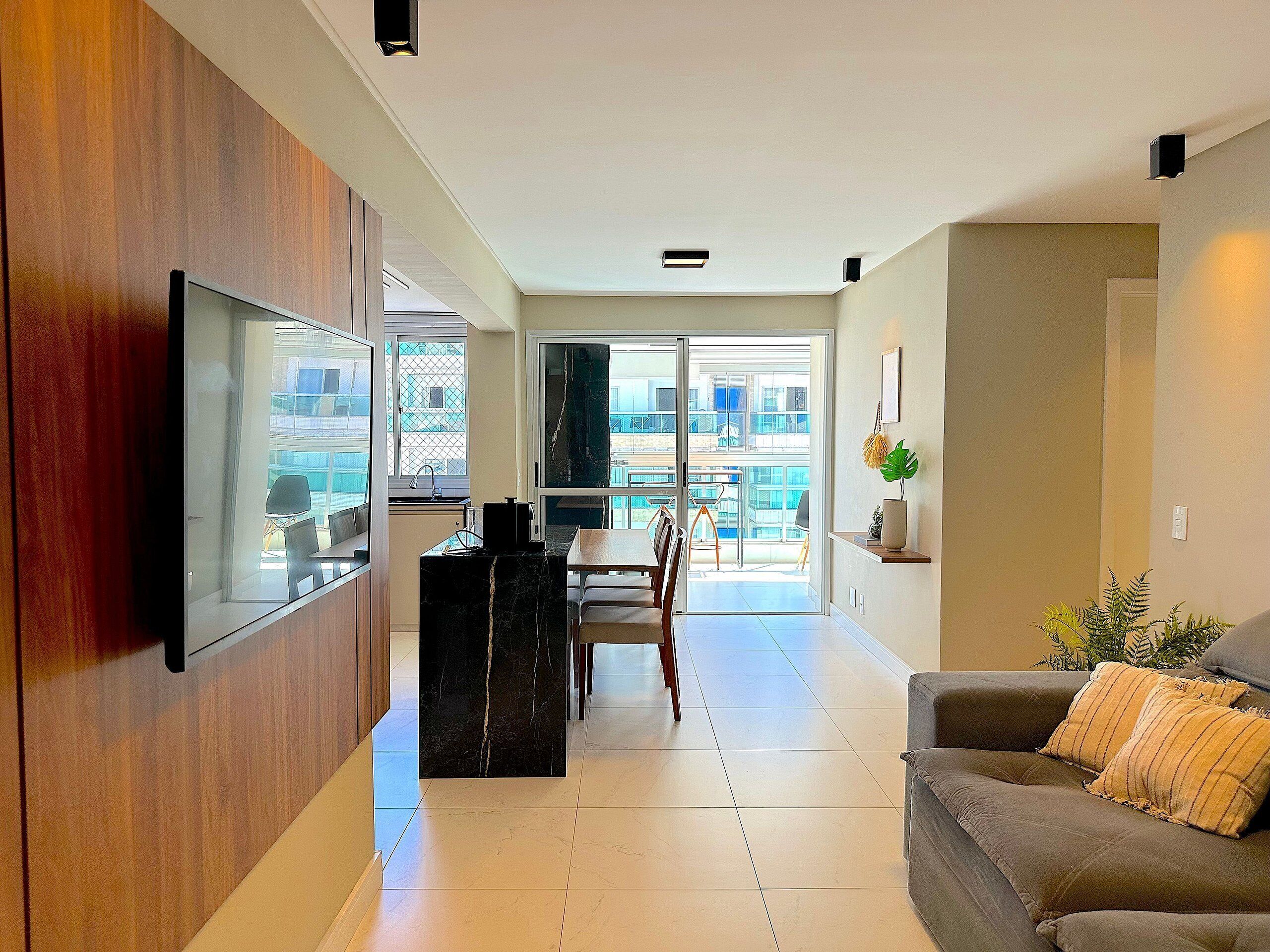 A modern living room with a flat-screen TV, a dining area, and a balcony with a view.