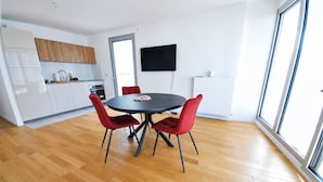 Eine moderne Küche mit weißen Schränken, eine Essecke mit rundem Tisch und roten Stühlen sowie ein großes Fenster, das natürliches Licht hereinlässt.