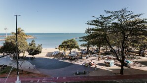 Uma área à beira-mar com calçada pavimentada, árvores e vista clara do mar.
