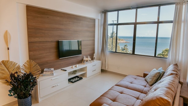 Uma sala de estar moderna com uma janela ampla, uma TV de tela plana, um sofá e uma planta decorativa.