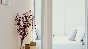 Quarto de hotel moderno com um espelho grande, mesa de cabeceira com um vaso de flores secas e uma cama bem arrumada.