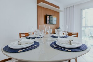 Ein Esstisch ist gedeckt mit Tellern, Besteck und Gläsern, mit einer Holzwand und einem Fernseher im Hintergrund.