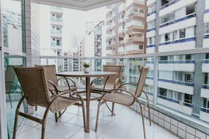Ein Balkon mit Korbstühlen und einem Tisch, der auf einen Stadtblick mit Hochhäusern blickt.