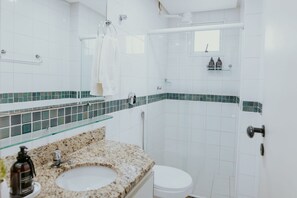 Ein Badezimmer mit Waschbecken, Toilette, Dusche und einer Glasablage für Toilettenartikel.
