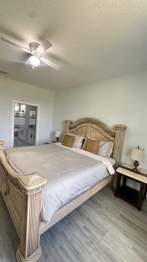 A bedroom with a large bed, a ceiling fan, a nightstand, and a bathroom visible through an open door. - The Grey House (Palm Bay)
