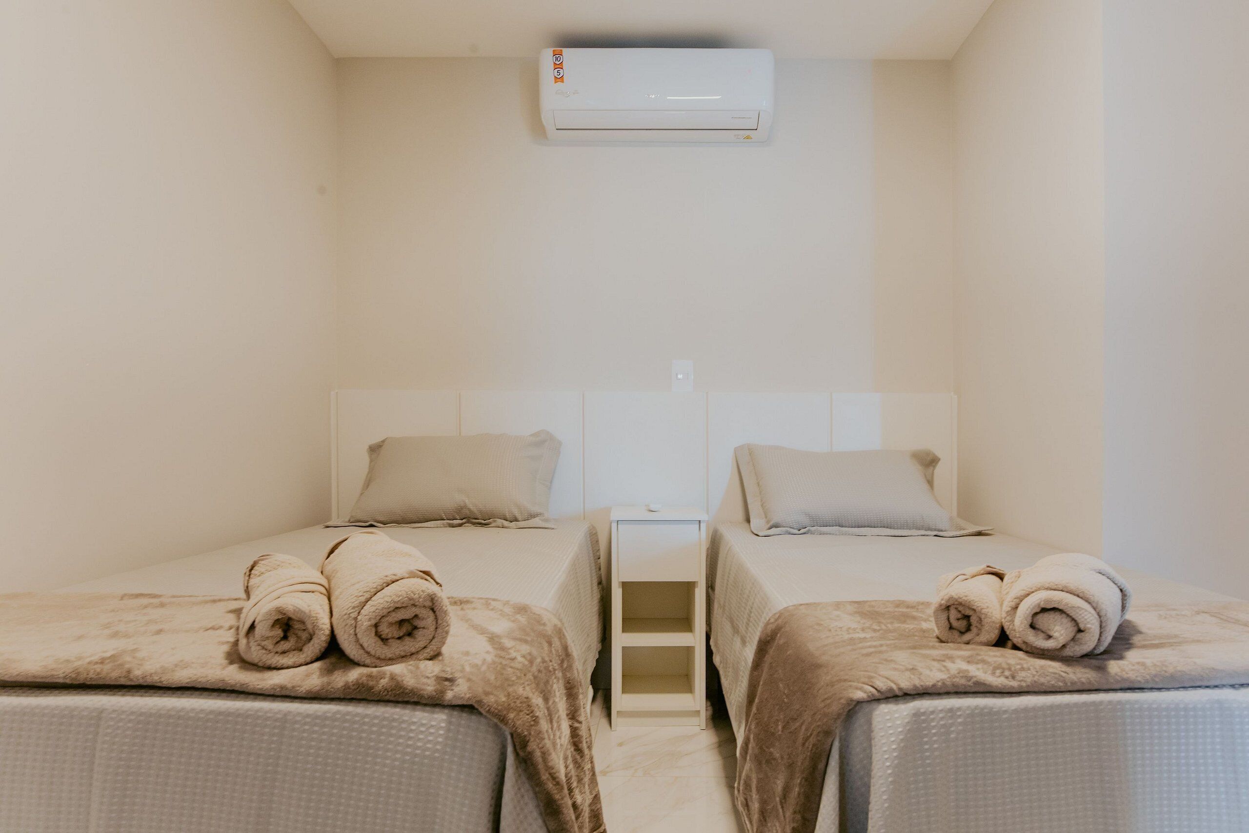 Ein Hotelzimmer mit zwei Betten, einer weißen Klimaanlage und einem kleinen Nachttisch.
