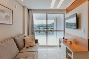 Ein modernes Wohnzimmer mit einer Couch, einem Flachbildfernseher, einem Holztisch und einem großen Fenster mit Blick auf die Stadt.
