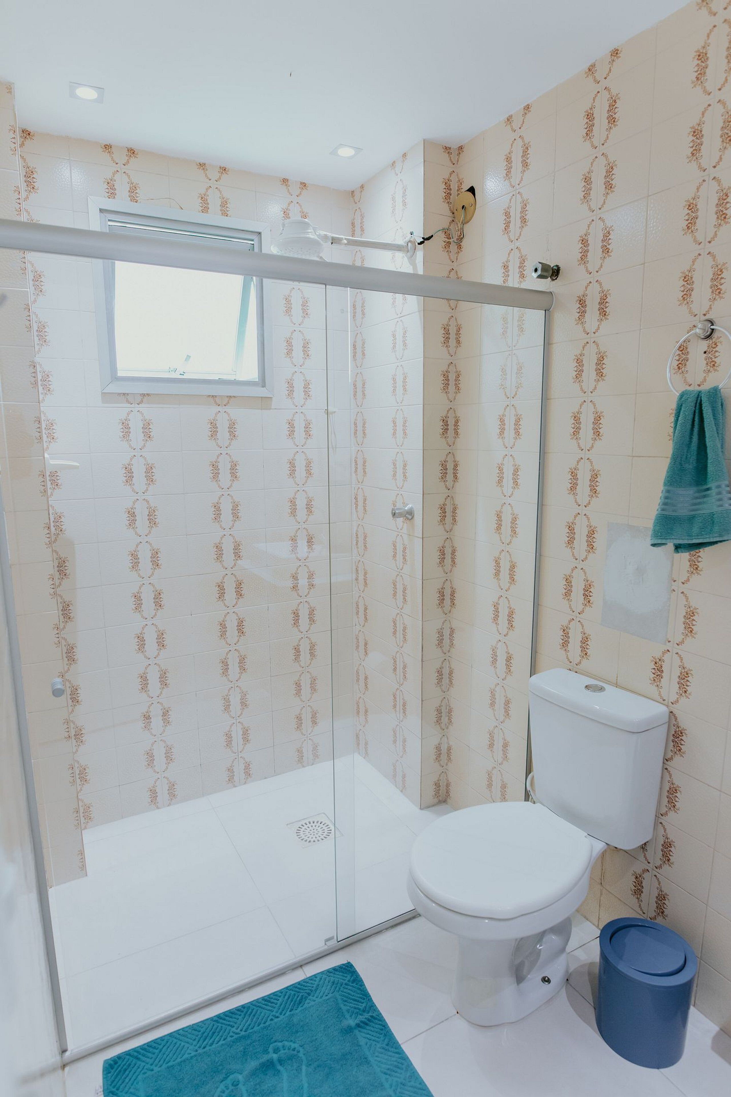 A bathroom with a glass shower enclosure, a toilet, and a blue trash bin.