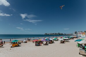 Ein Strand mit Sonnenschirmen, einem Wagen und einer entfernten Skyline einer Stadt.