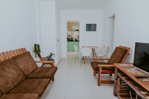 Ein Wohnzimmer mit braunem Sofa, einem Fernseher und einem Essbereich mit Tisch und Stühlen.