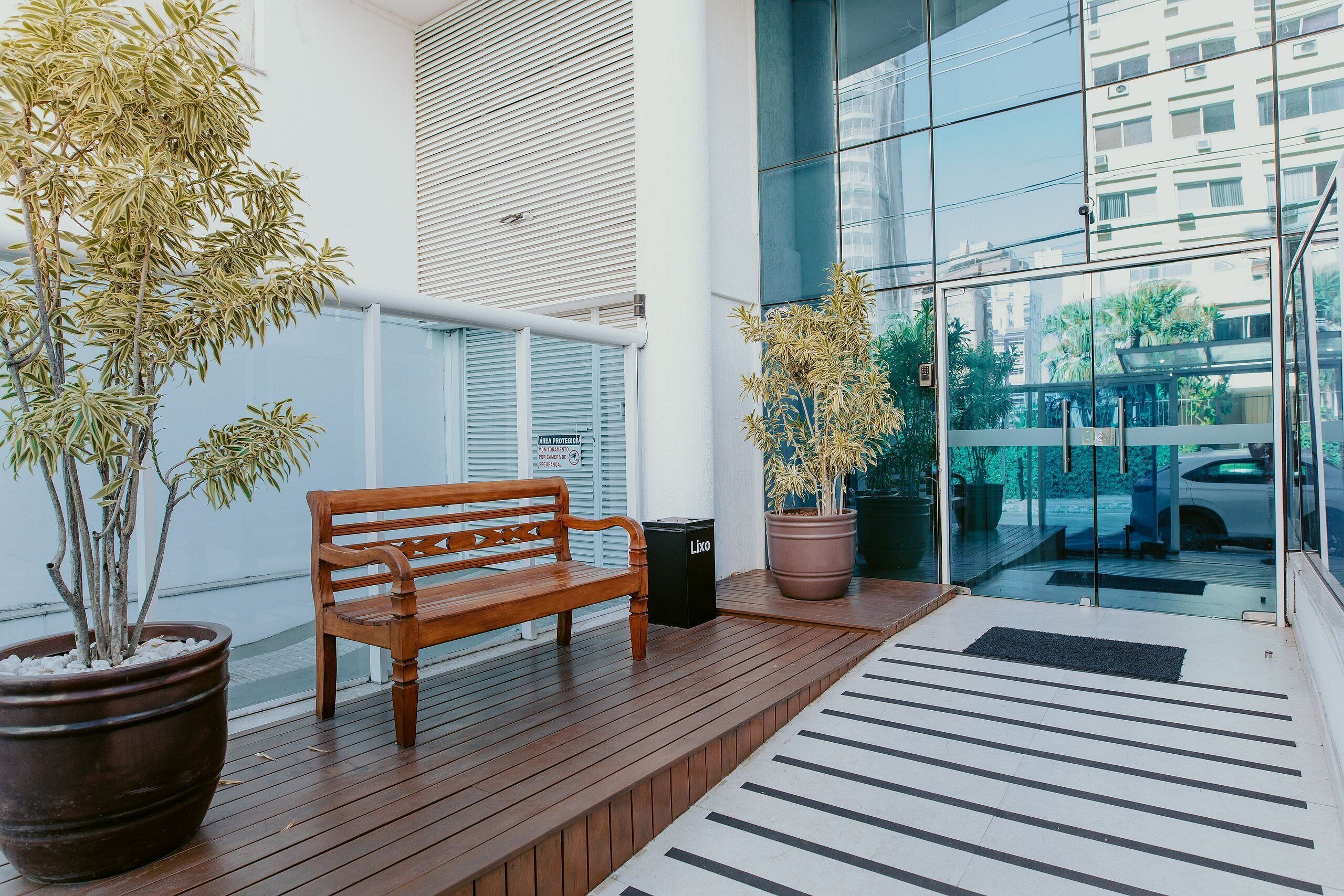 A wooden bench, potted plants, and a glass door leading to a balcony with a view of buildings.