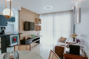 Eine moderne Küche mit Einbauofen, ein Essbereich mit rundem Tisch und ein Wohnbereich mit Sofa und Couchtisch.