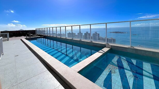A rooftop pool with a city view, clear sky, and sun. - Modern apartment with incredible sea views (Vila Velha)