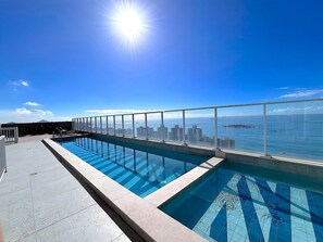 Pool på taget med udsigt over byen, klar himmel og sol.