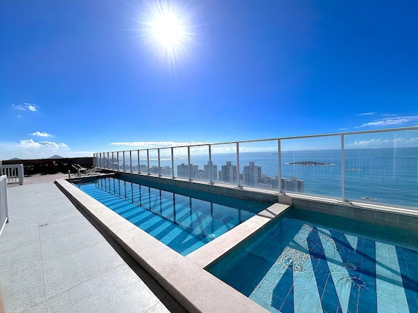 Ein Pool auf dem Dach mit Blick auf die Stadt, strahlend blauer Himmel und Sonne.