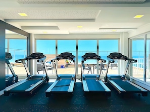 Ein Fitnessstudio mit Laufbändern und großen Fenstern mit Blick auf einen Strand.