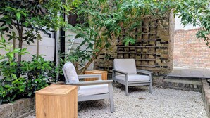 An outdoor seating area with two chairs and a wooden table, surrounded by gravel and greenery. - Be London - The Hampstead Residences (Greater London)